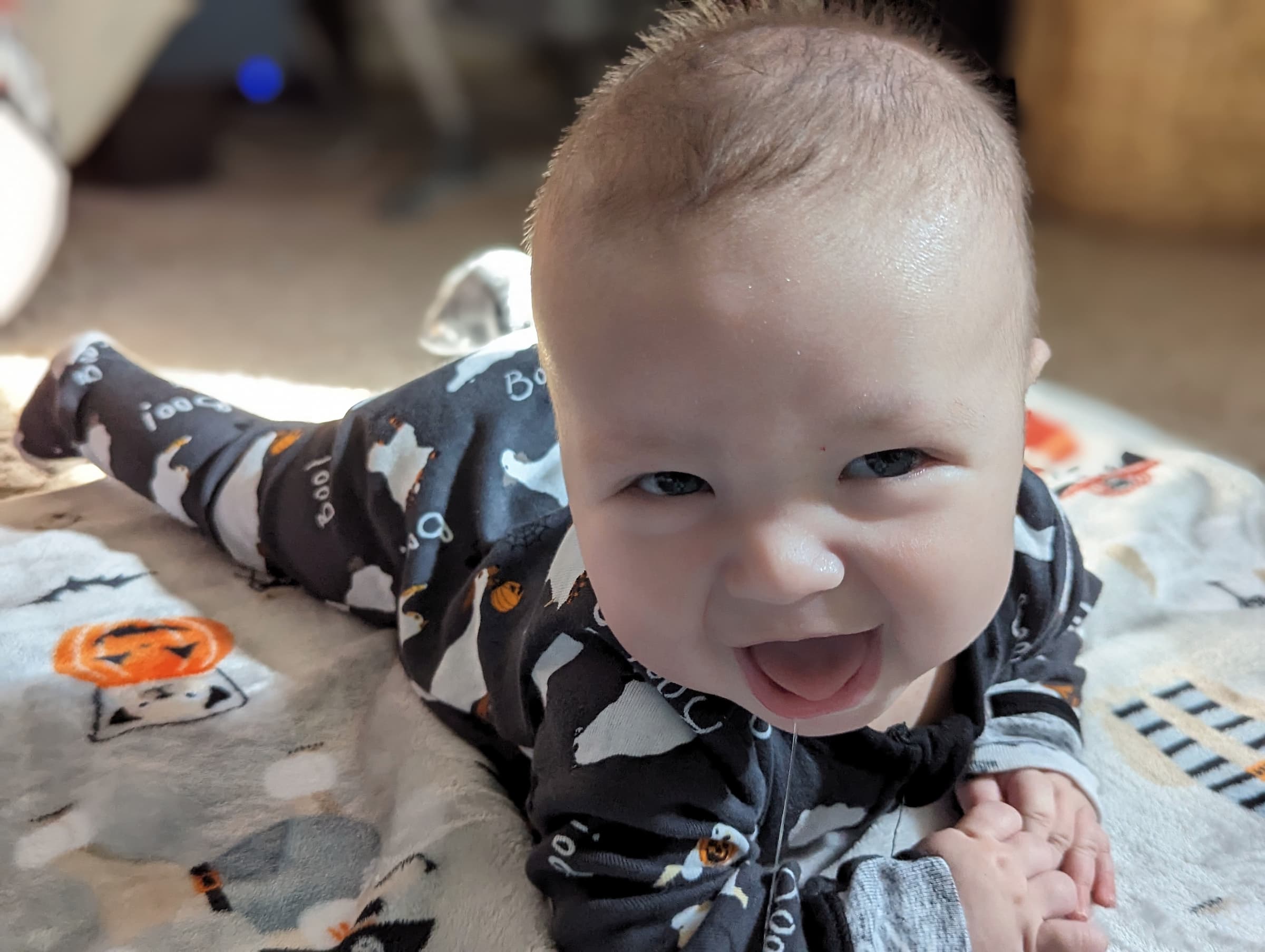 A baby wearing black pajamas, with dogs dressed as ghosts on it, looking at the camera with a goofy grin.